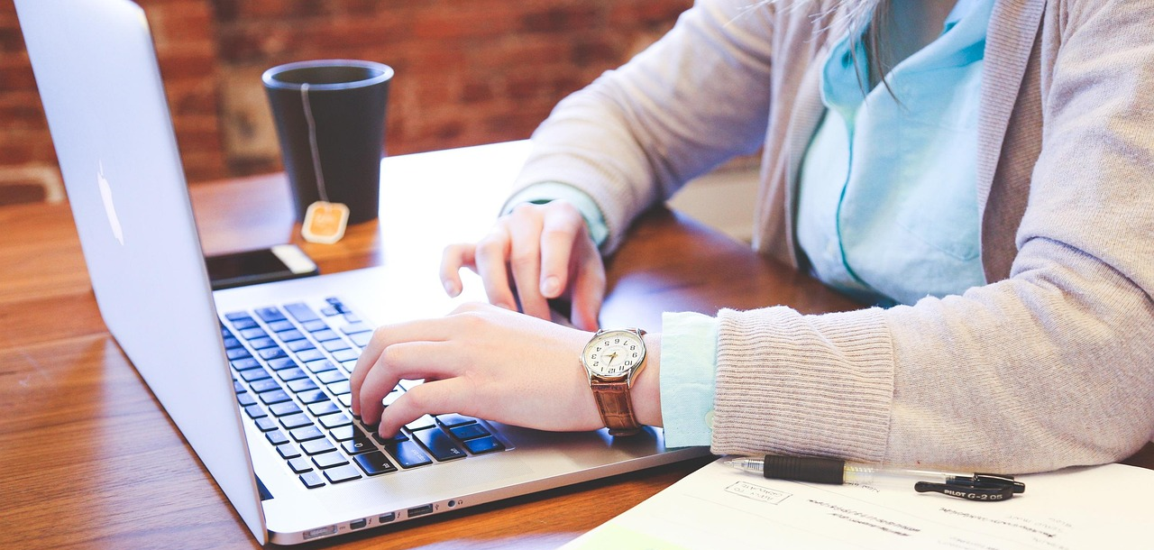 Woman working on her laptop at a desk with a cup of tea beside her.